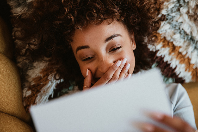 Woman lying and reading a letter on a couch